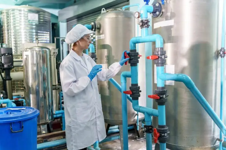 Woman in lab coat checks valves in industrial water treatment facility