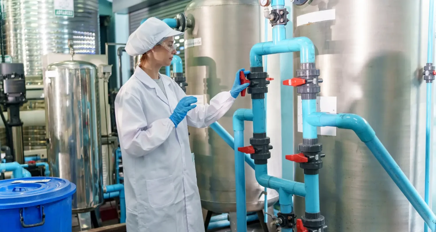 Woman in lab coat checks valves in industrial water treatment facility